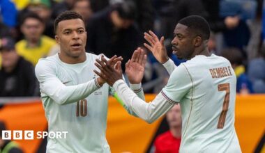 Kylian Mbappe (left) and Ousmane Dembele (right, photographed from behind), both wearing white France shirts, high five one another