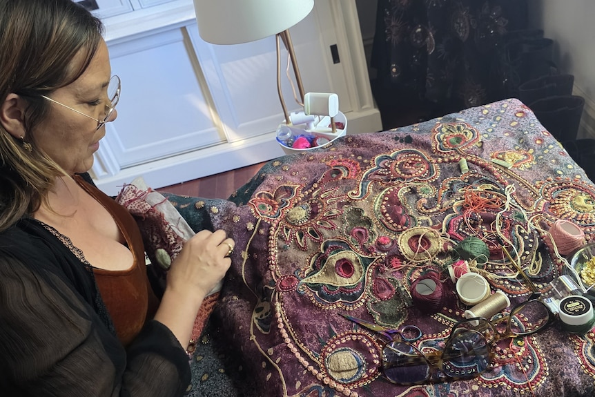 Lady sewing with cotton spools and a bowl of sequins on the quilt.
