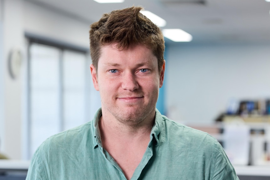 A man in a green shirt stands in an office.