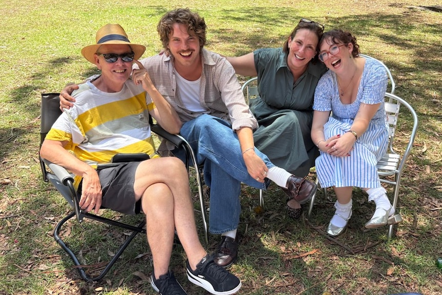 A mother and father with their adult daughter and son sitting outdoors on the grass on camping chairs, all smiling