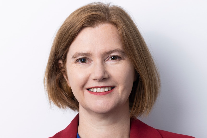 A young woman with a light coloured bob smiles, she's wearing a bright blue top and a bright red blazer.