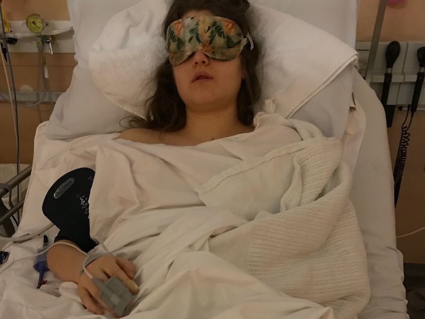 A girl lies in bed with eyes covered.