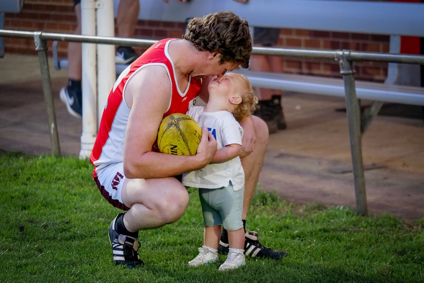 A man in football training clothes cuddles a small child