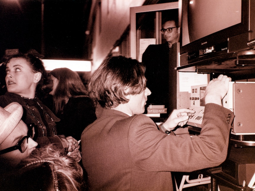 Black and white man back facing away has hands on wiring and electronics
