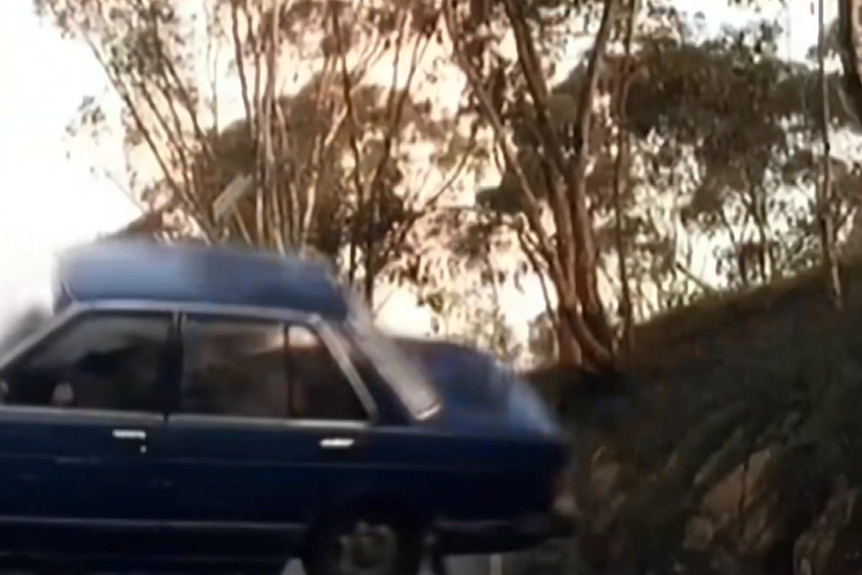 A depiction of a blue car on its side on a road.