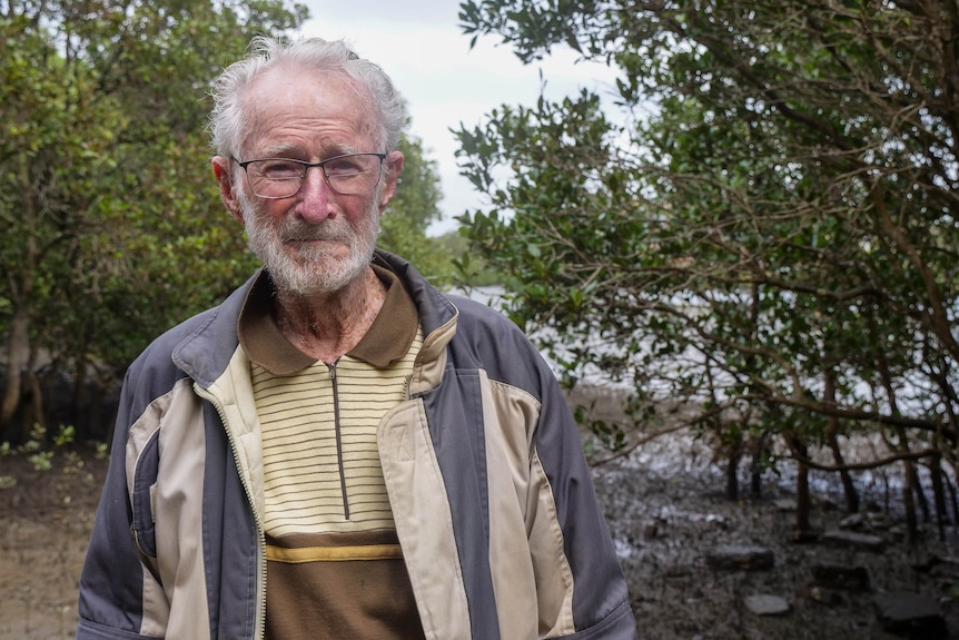 an elderly man standing by the shore of a bay