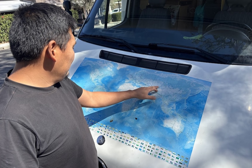 A man looks at a printed map of the world and points out a destination.