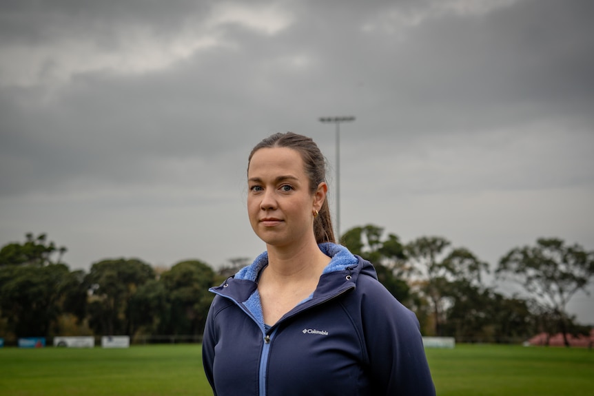 A woman stands with her hands behind her back on a football field
