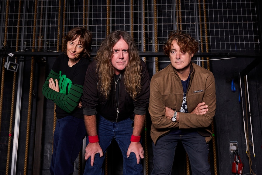 middle-aged woman and two middle-aged men pose in jeans and casual wear backstage at theatre