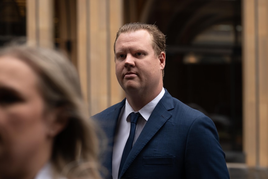 A man with slicked back hair in a blue suit and tie.