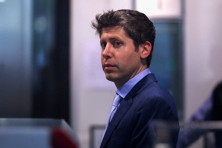 A close up of Sam Altman in a business suit standing and looking over his shoulder.