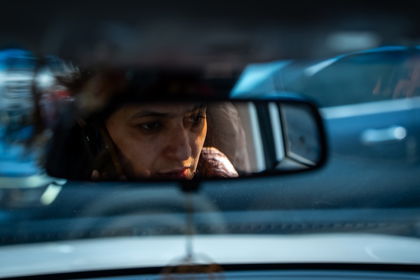 A woman's reflection in a car's rearview mirror.