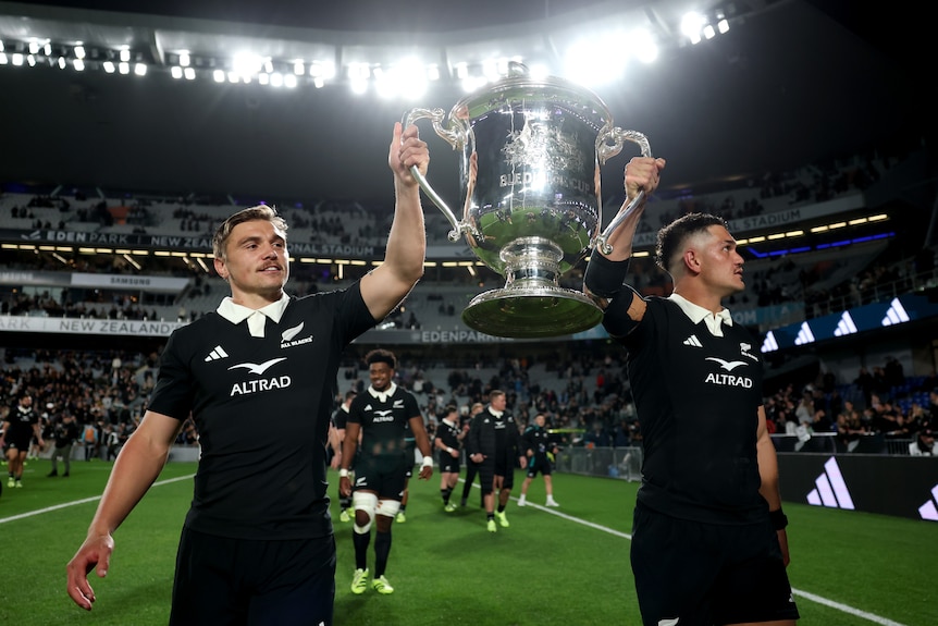 Two All Blacks players hold up the Bledisloe Cup.