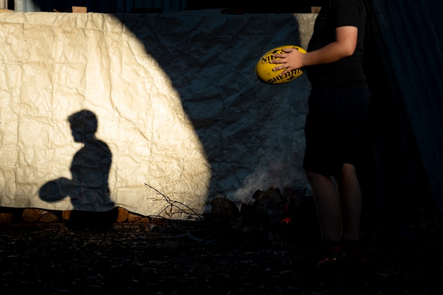 A shadow of a young boy playing AFL football in his backyard
