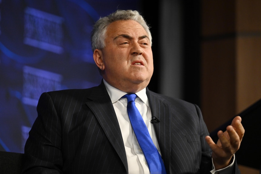 Hockey gestures with one hand, sitting on the national press club stage.
