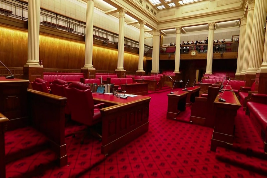 A parliamentary chamber with red seats, carpet and desks