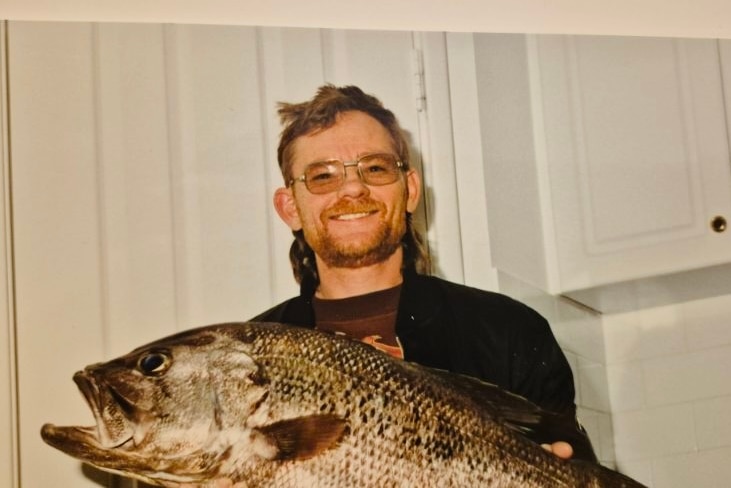 A man smiles while holding a large fish