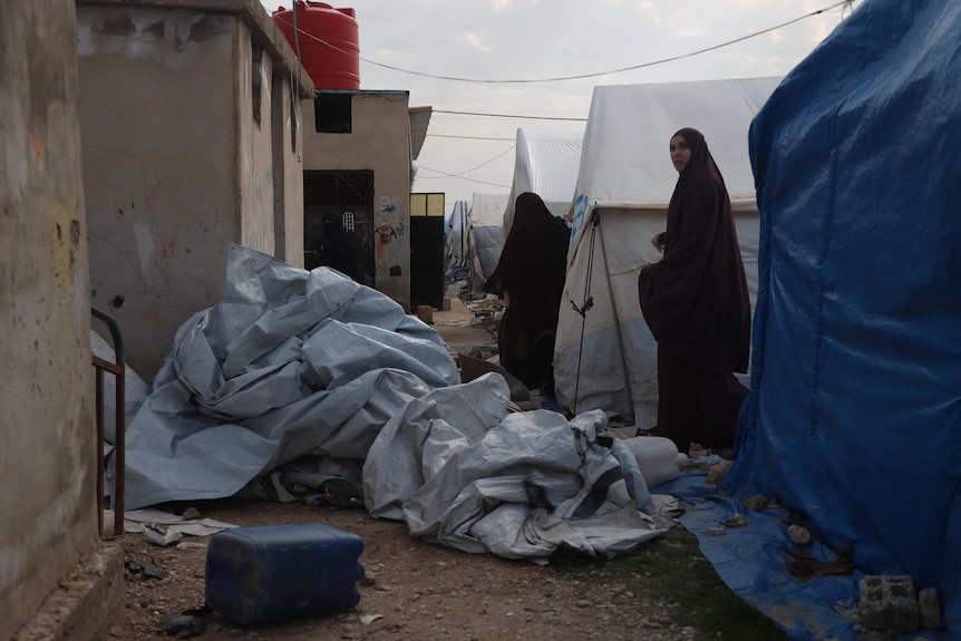 Two women walking alongside tents in a laneway with a crumpled tarpaulin in the centre.