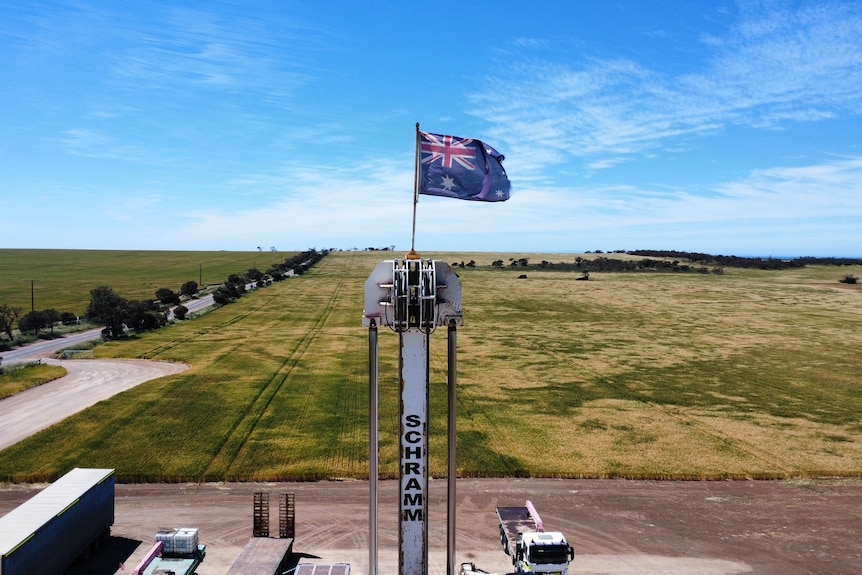 An Australian flag atop a drilling rig, with grassy fields behind it
