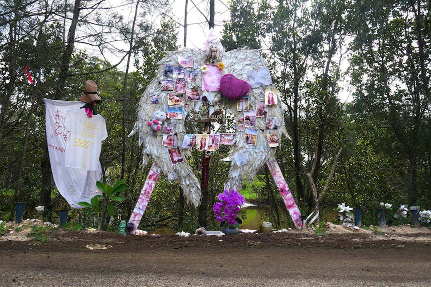 A roadside memorial featuring large angel wings covered in photos and other memorabilia