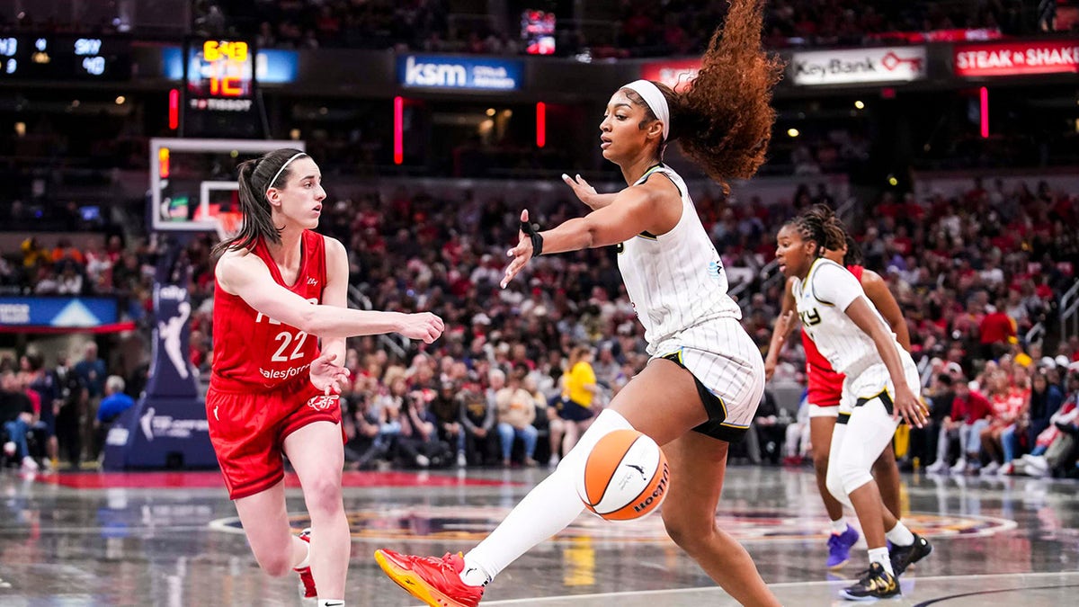 Indiana Fever guard Caitlin Clark passing basketball around Chicago Sky forward Angel Reese at Gainbridge Fieldhouse