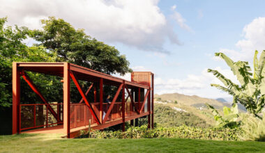 red elevated metal walkway extends casa castela across steep brazilian slope