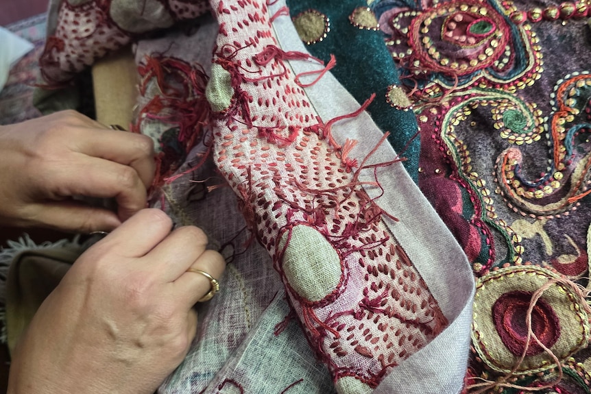 A close up of hands handsewing a colourful pattern on fabric.