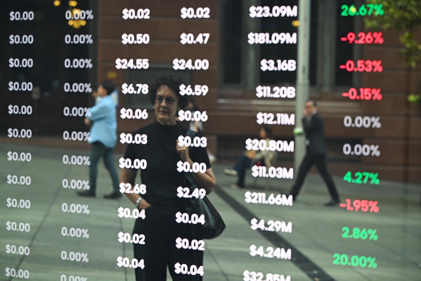 A woman is seen reflected in a screen showing stock information