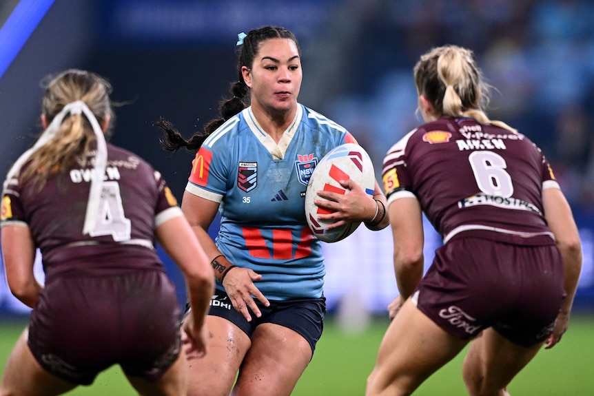 A women's rugby league player in Blues uniform running at two Maroons defenders.