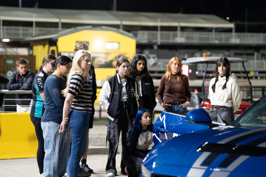 A group of young women stand next to a blue car at Sydney motorsport park.