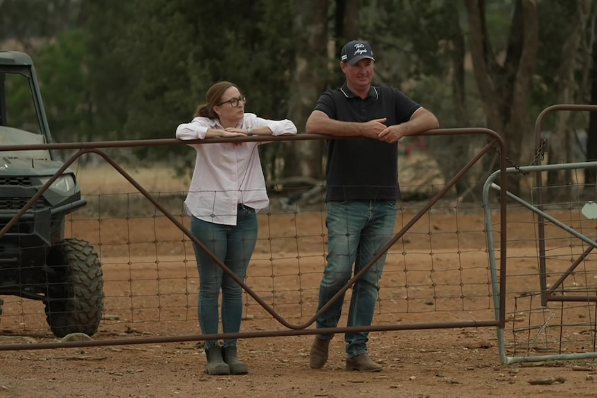 A man and a woman leaning on a fence.