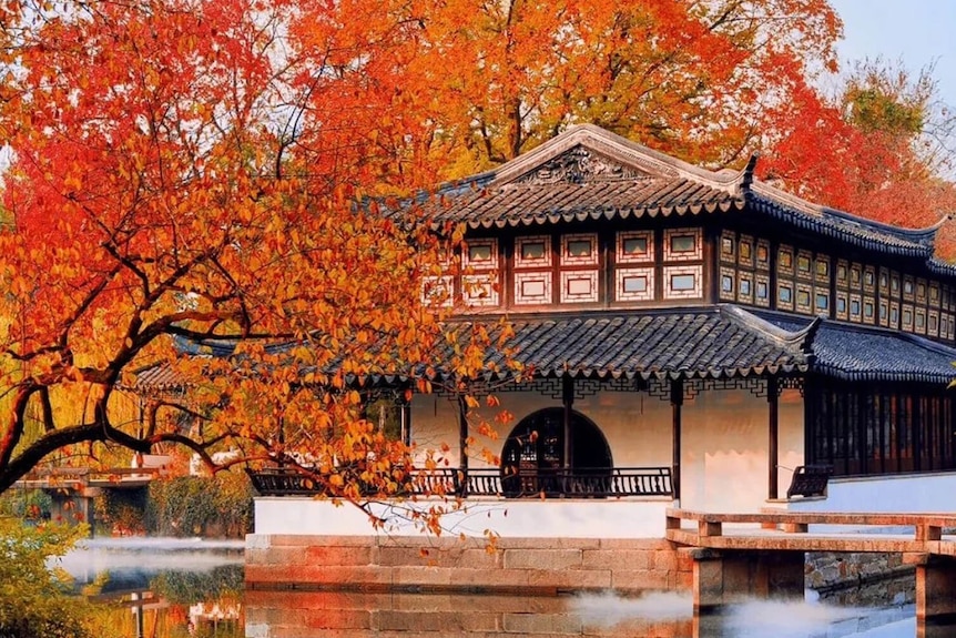 A traditional Chinese building beside a lake and trees in red autumn colours.