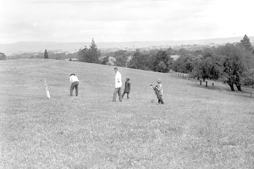 A black and white image of golfers, trees in the background.