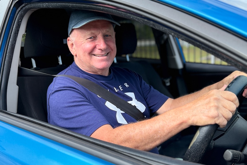 Man in blue shirt and hat in blue car smiling