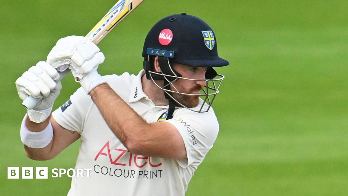 Ben Raine wearing a helmet with a Durham badge on it swooshes his bat high above his shoulder