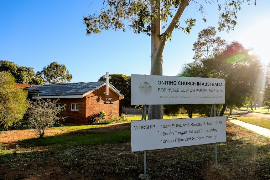 A sign reading UNITING CHURCH OF AUSTRALIA in front of a brick building with a white crucifix