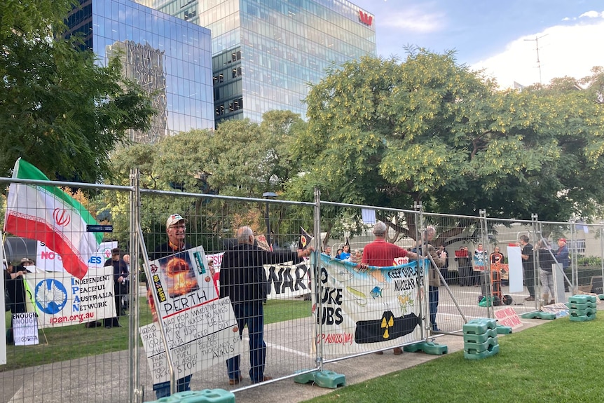 More than a dozen people stand on a lawn holding anti-war banners and flags.