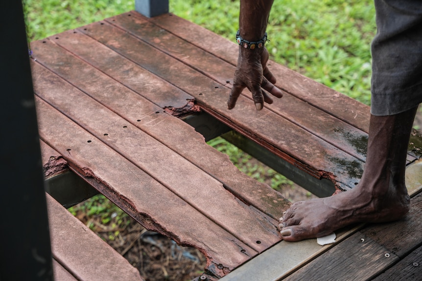 A broken timber deck with an Aboriginal person pointing to the holes