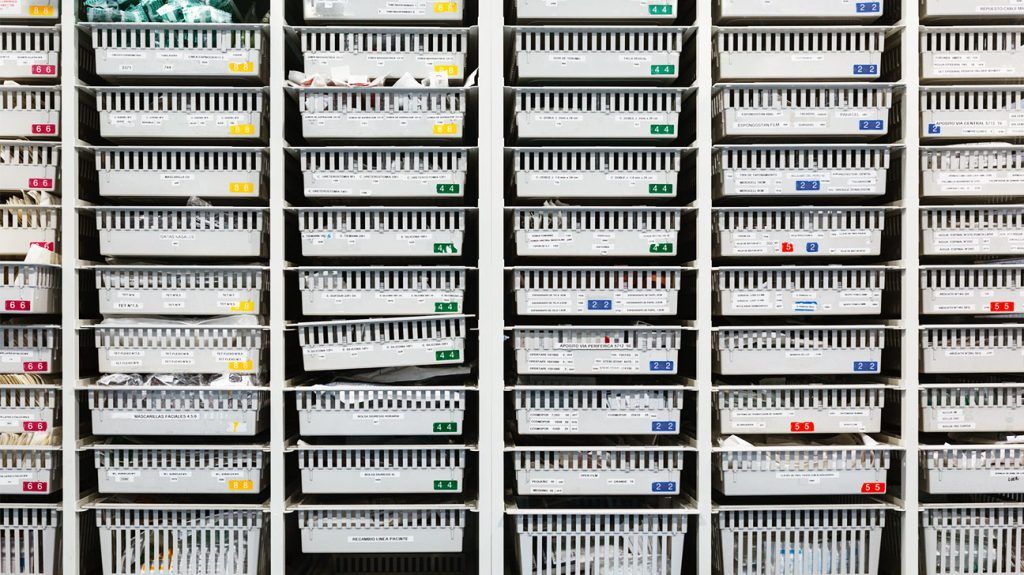 Rows of labeled white storage bins filled with medical supplies organized on tall shelving units.