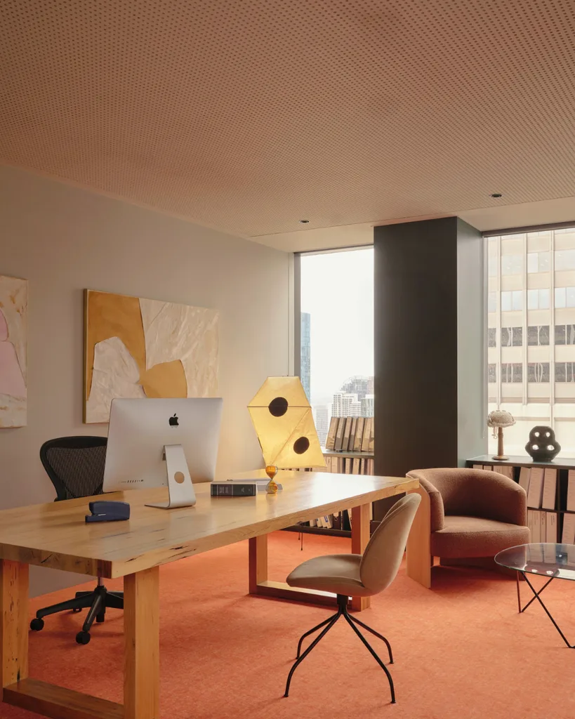 Modern study with pink carpet, timber desk, leather arm chair and view from window of city