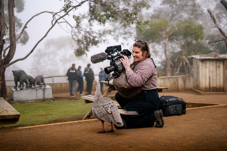 A woman holding a camera filming a goose