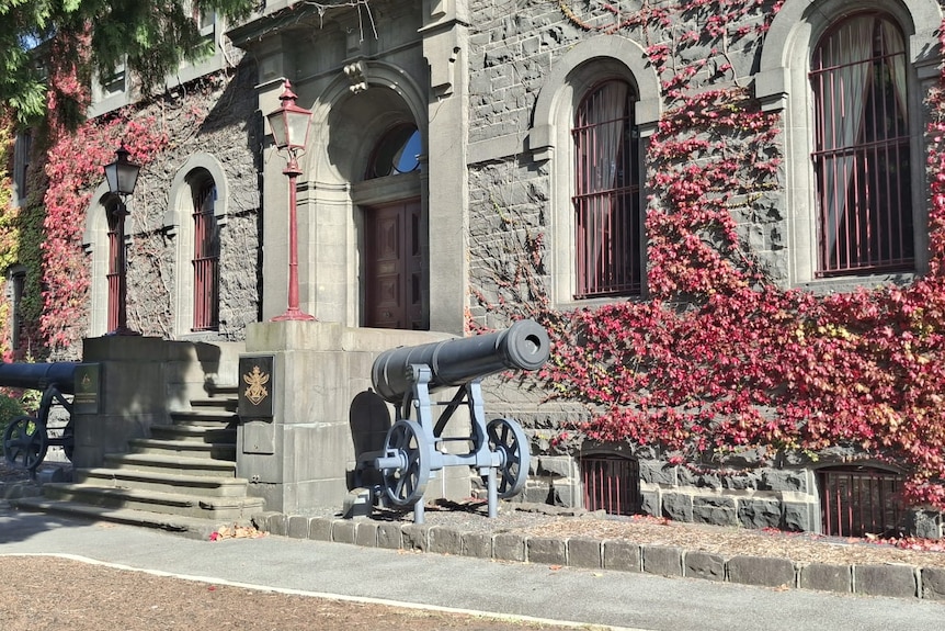 Front of a bluestone budiling covered in ivy with a military canon on either side of the front door.