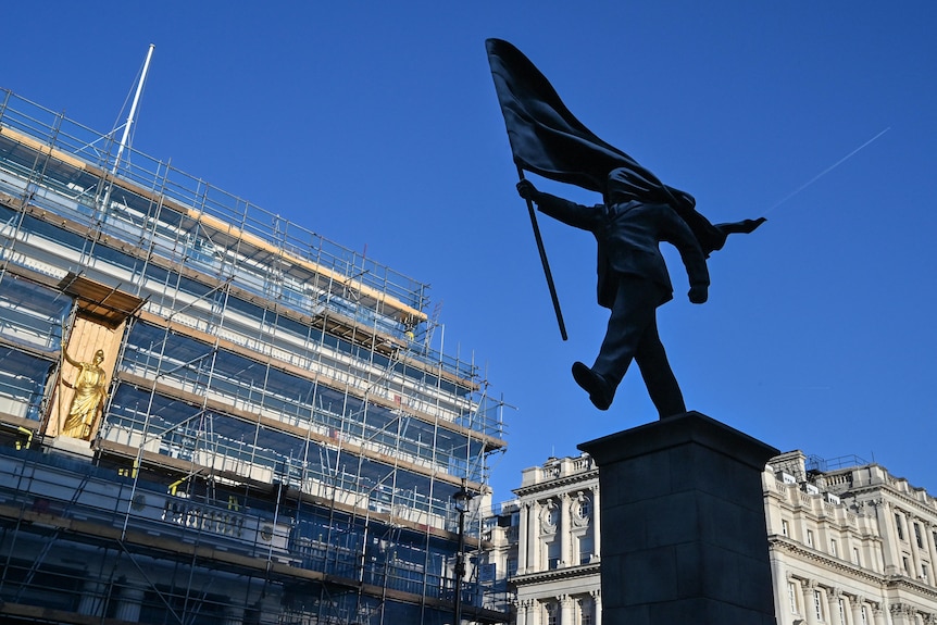 A statue of a man, mid stride, walking forward carrying a flag, a blind fold across his face. 