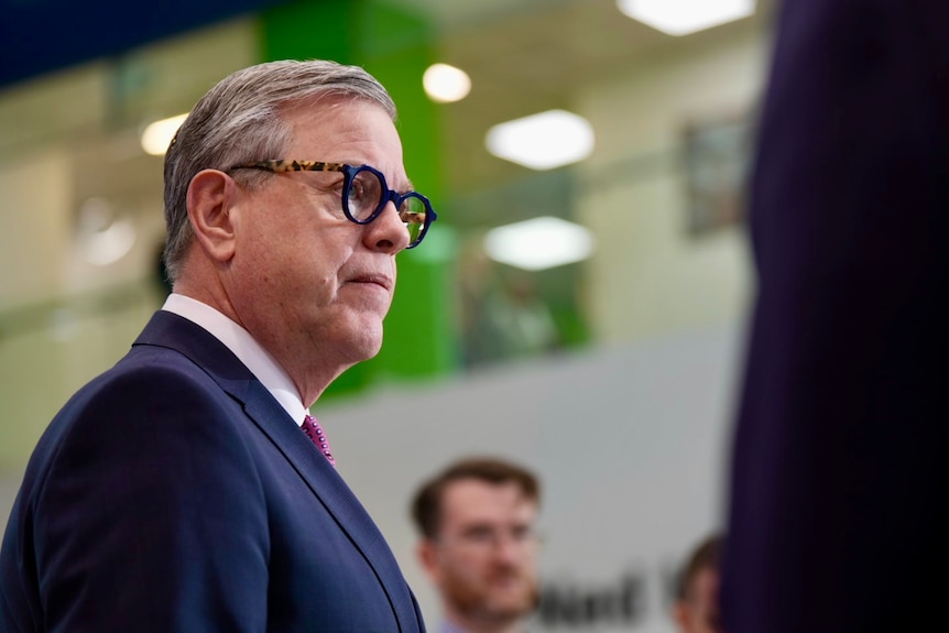 A man with grey hair and glasses speaks to reporters at a press conference