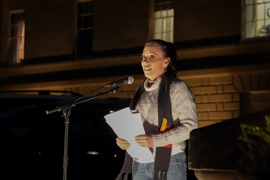 Nala Mansell with an Aboriginal flag scarf, speaking at a vigil.