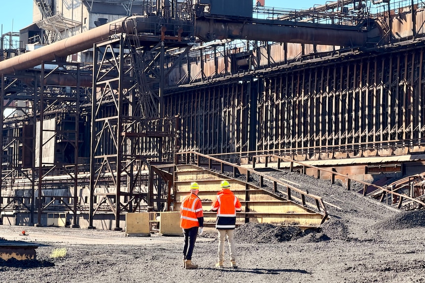 Two men stand looking at a large industrial building