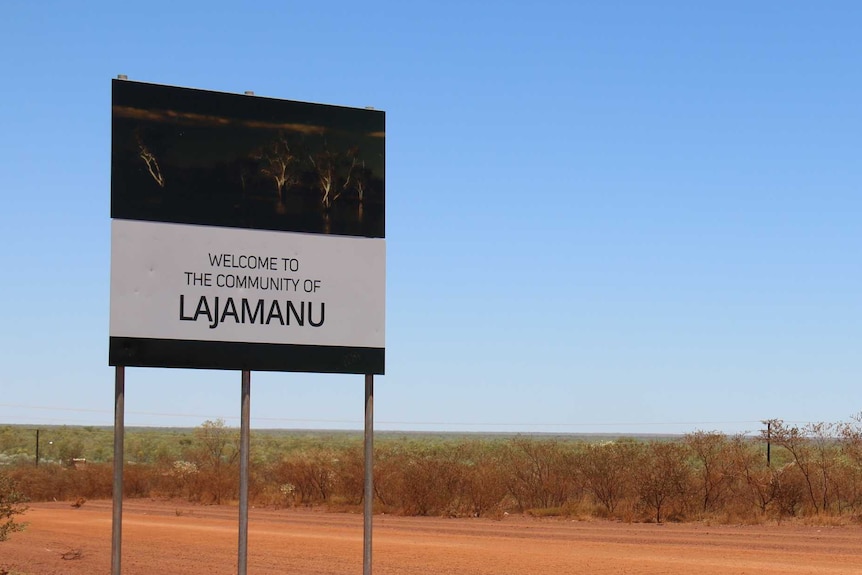 Red dirt country, with a single black-and-white sign in view, to the left of frame that reads 'Lajamanu'
