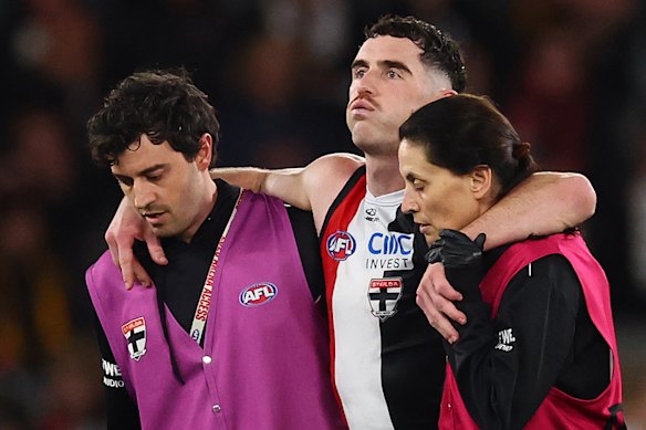 Sam Flanders is helped from the Marvel Stadium surface by the Saints trainers.