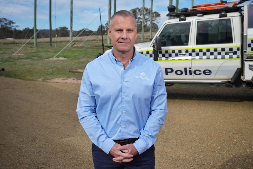 A man wearing a light blue shirt behind a police vehicle. 