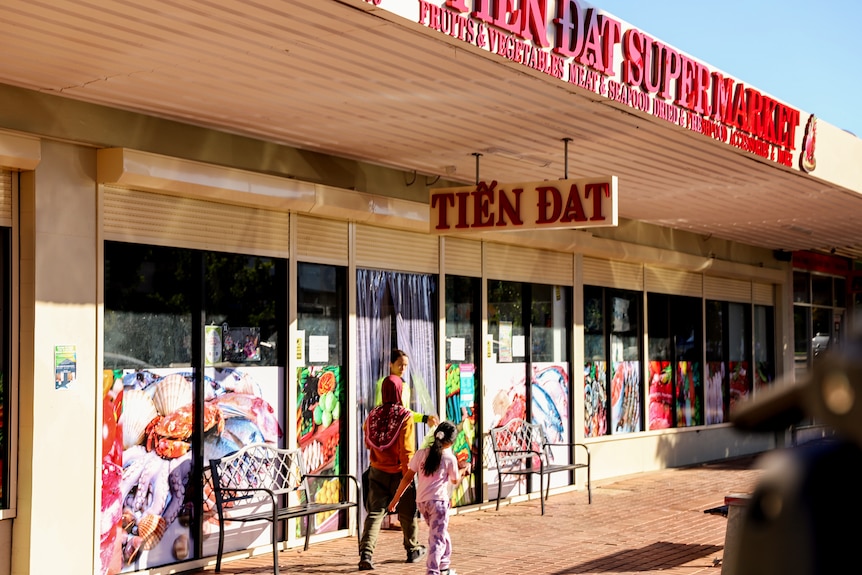 a street with people walking in front of a store that has a sign reading 'Tien Dat Supermarket'